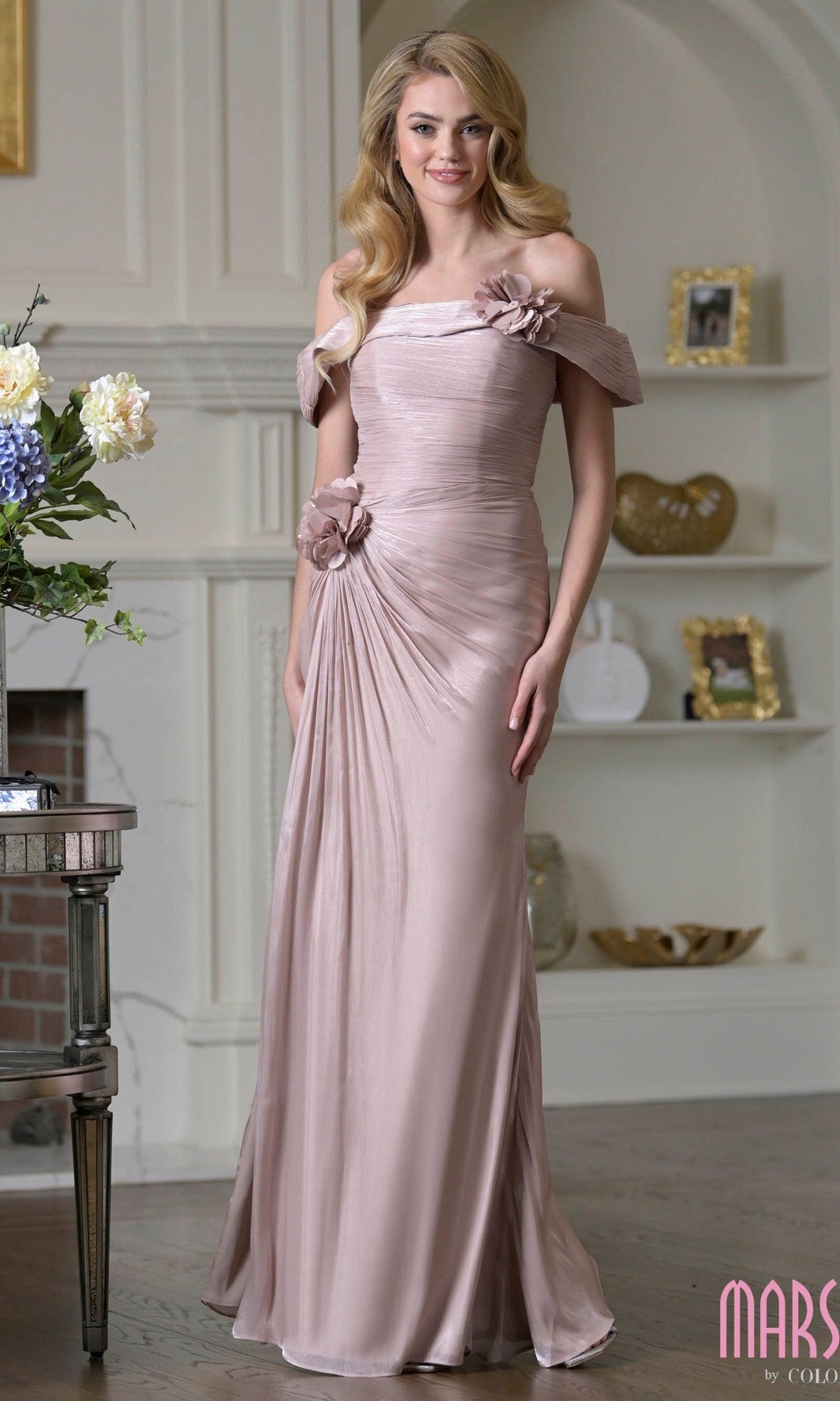 A woman stands indoors in the Marsoni M353, a floor-length mauve gown featuring off-the-shoulder crinkled chiffon, shimmer finish, and 3D floral accents at the waist and shoulder.